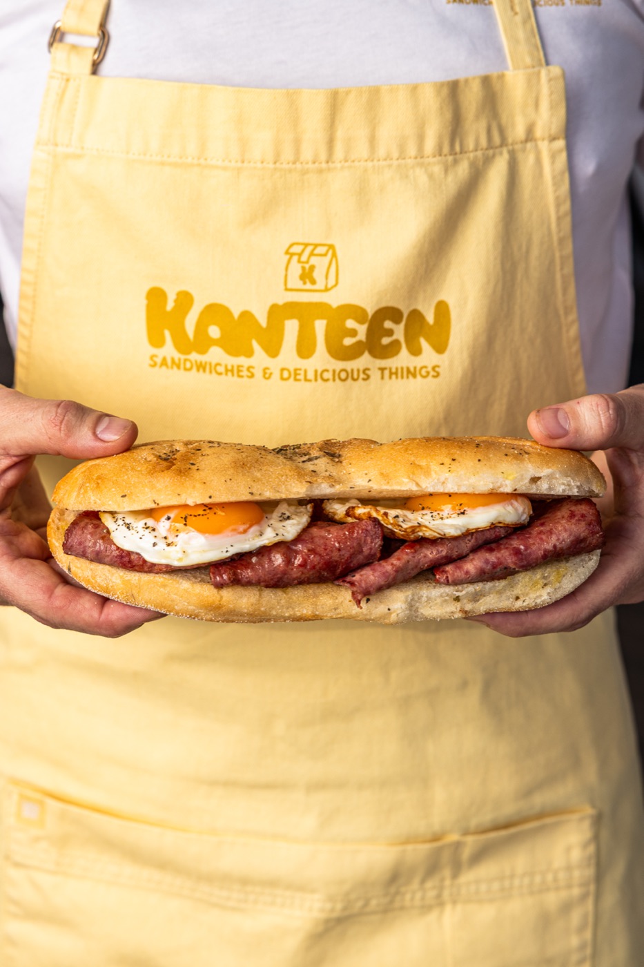 Kanteen sandwich held in front of a yellow Kanteen apron