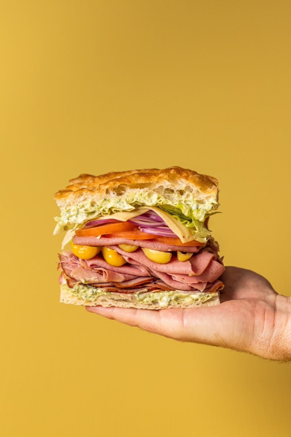 A hand holding a stacked ham and salad sandwich
